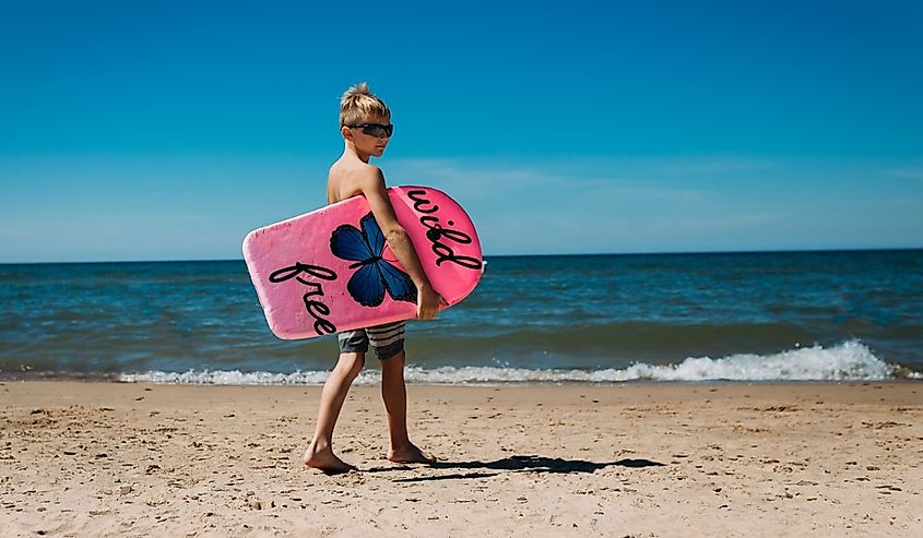 Boy with boogie board walking on beach toward Lake Michigan in Beverly Shores, Indiana.