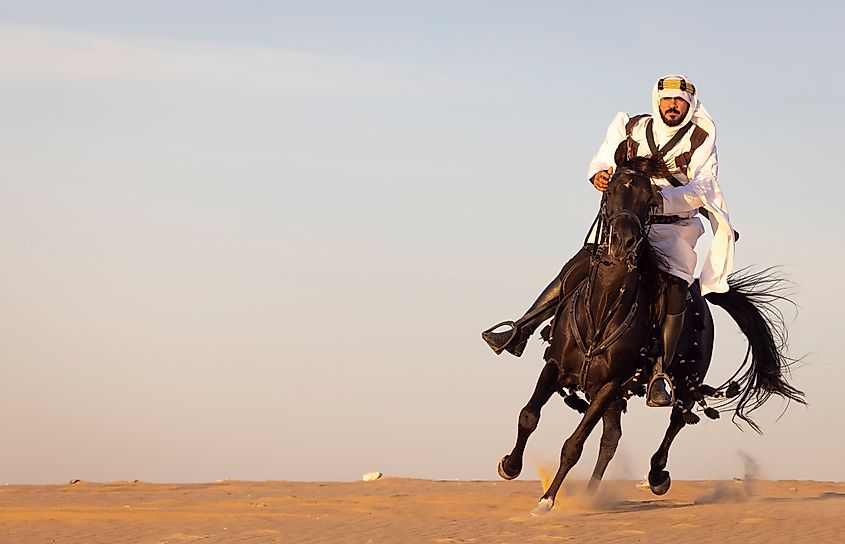 Saudi man in a desert with his black horse. Image Credit Katiekk via Shutterstock.