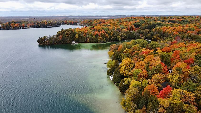 Vibrant fall colors around Elkhart Lake, Wisconsin, with red, orange, and yellow foliage surrounding the lake and reflecting off the calm waters.