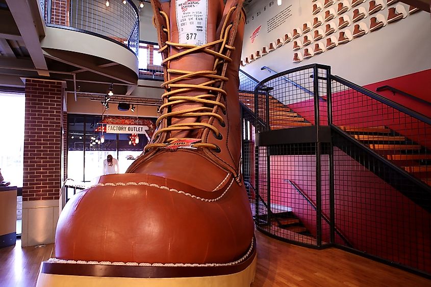 Giant brown leather boot with thick laces, displayed in a shoe store. A staircase curves around the boot, with colorful walls and lights.