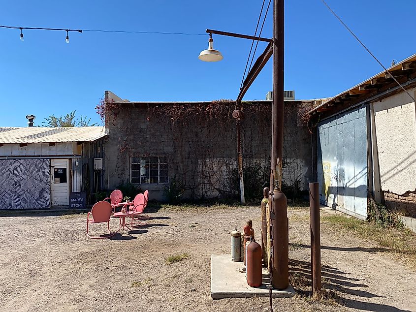 Old gas cylinders and lawn chairs strewn about a dusty and weathered courtyard. 