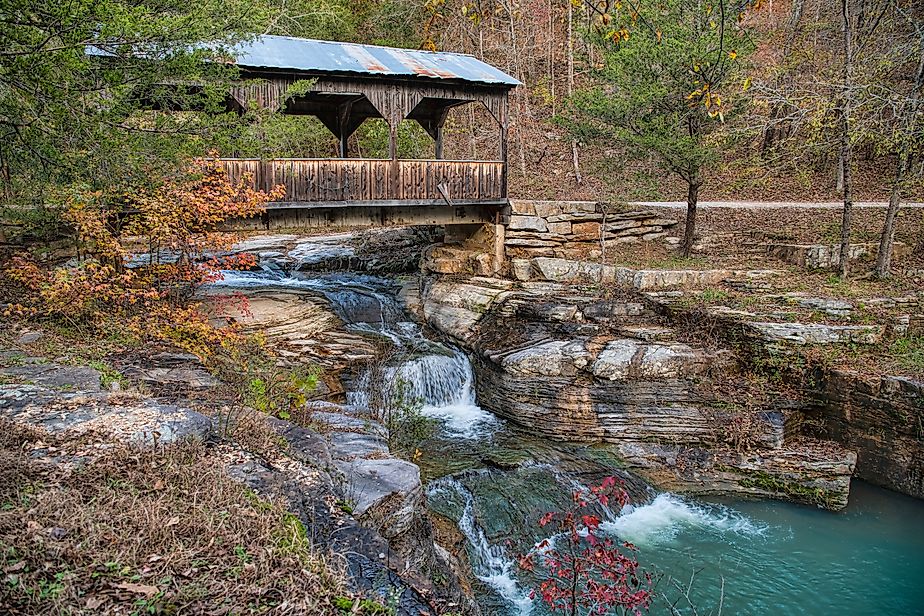 Covered bridge over cascading waterfall in fall in Ponca, Arkansas.