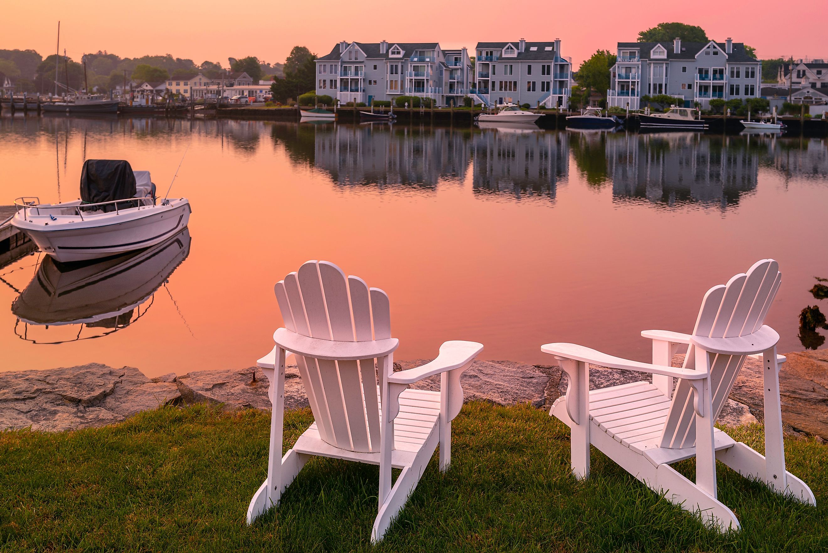 Sunrise with Adirondack chairs on the beach, moored boat, and smoke over Mystic River marina village, Connecticut.