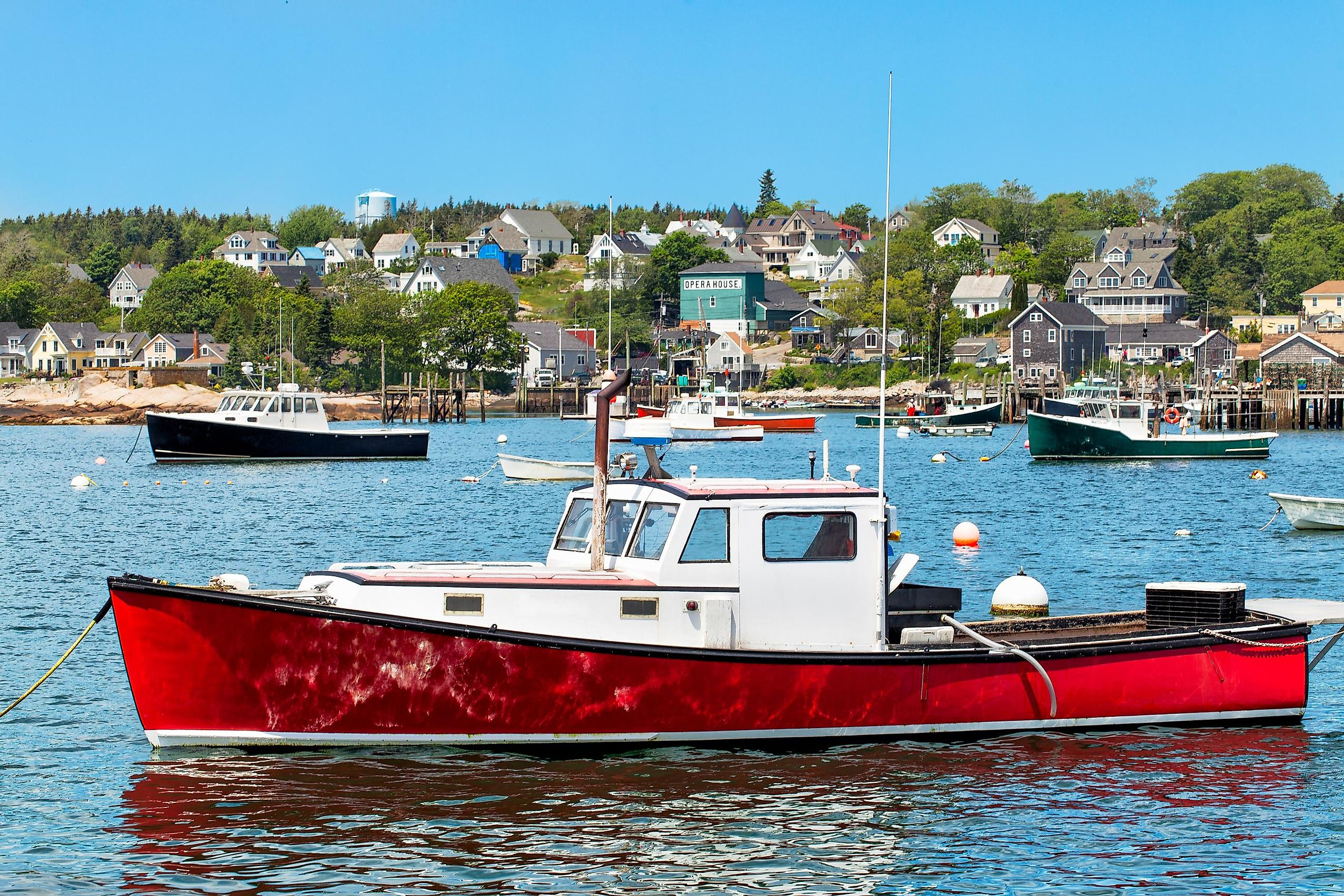 Harbor at Stonington, Maine, USA, features a vibrant red lobster boat in the foreground surrounded by scenic coastal beauty.