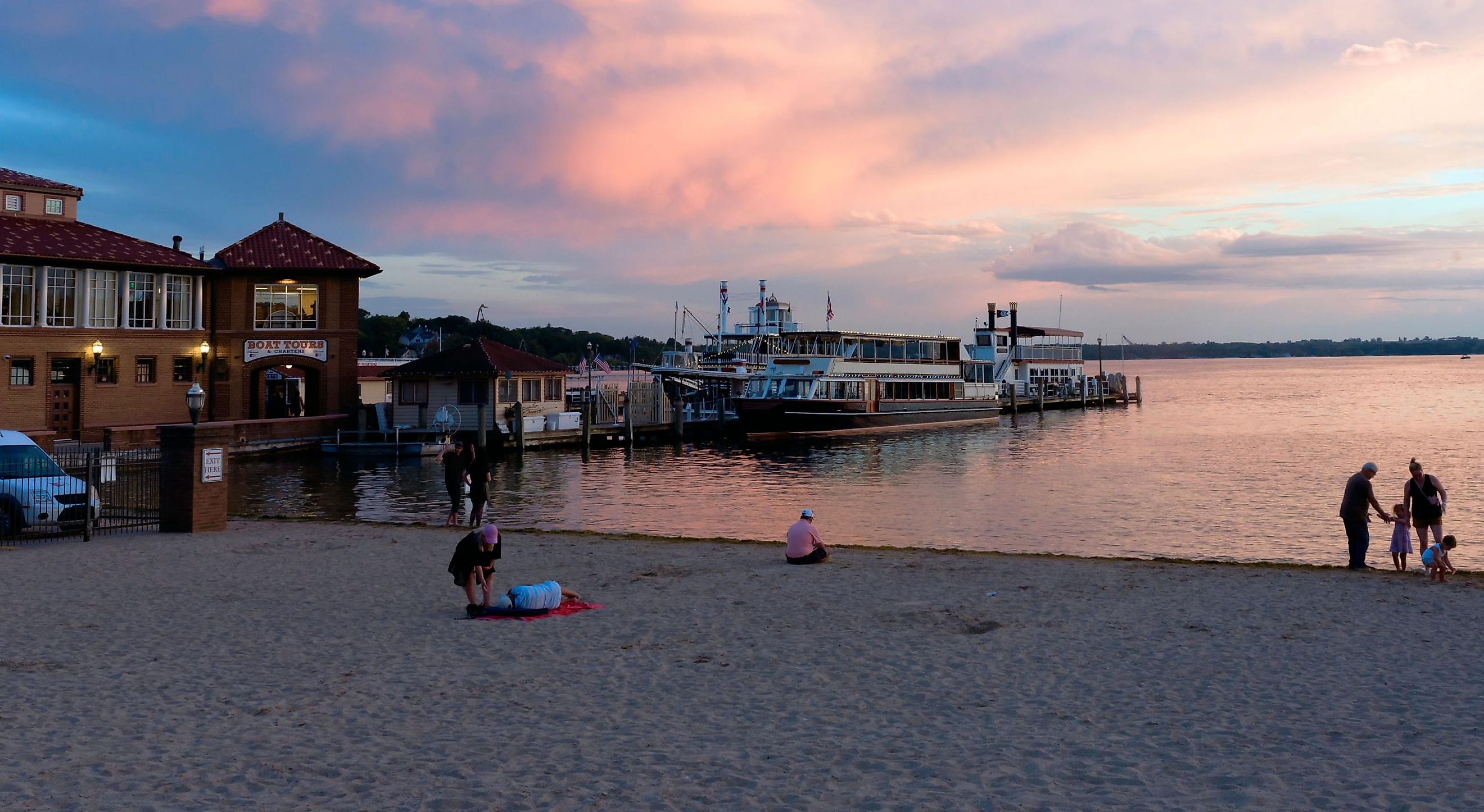 City of Lake Geneva, WISCONSINUSA-September 18, 2022: People gathering at the beach near Lake Geneva, showing the boat docks during a gorgeous pinky and cloudy sunset