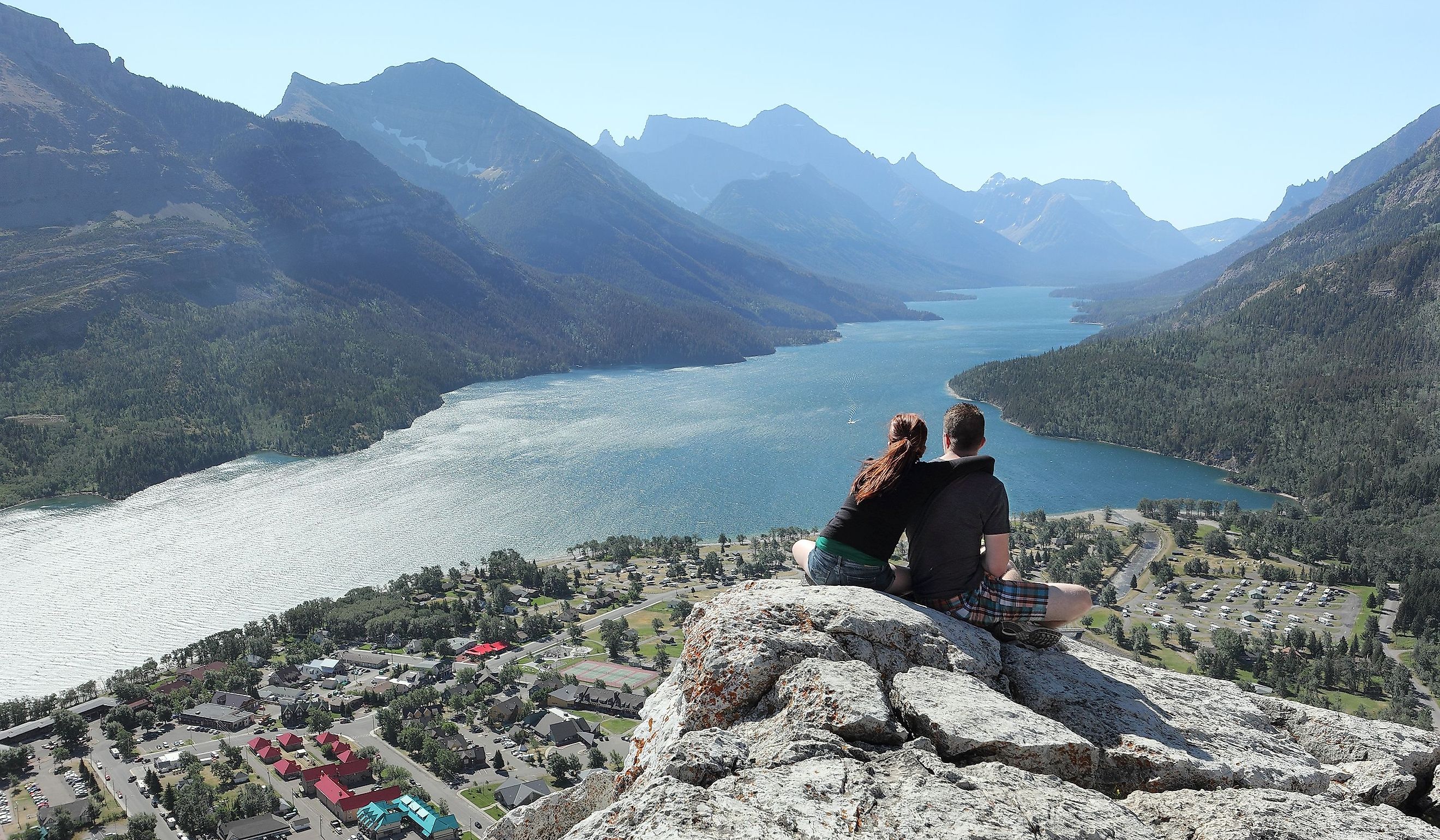 Couple With Elevated View of Town of Waterton, Alberta and a Mountain Lake - Waterton Lakes National Park, Canada.