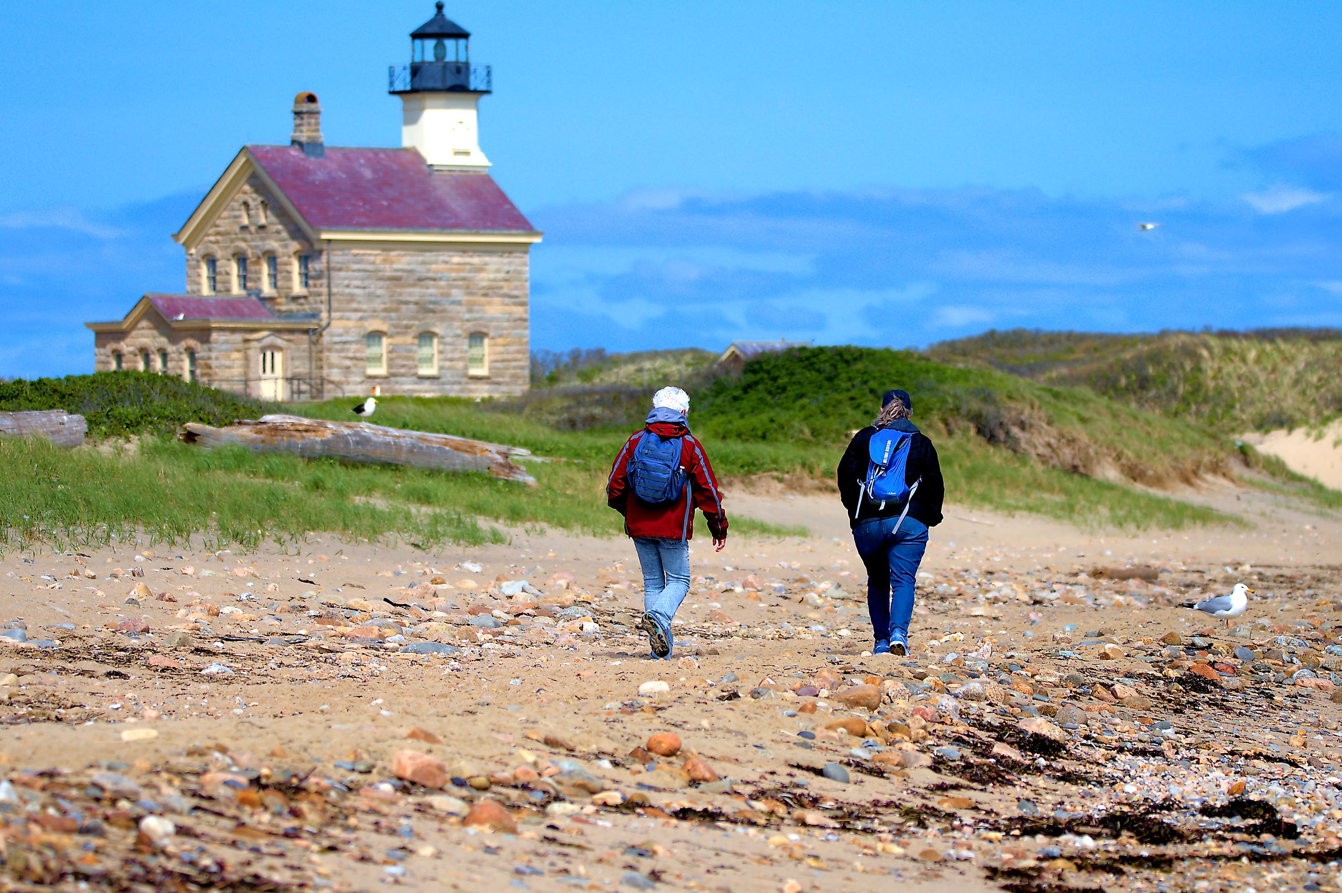 women walk the shoreline past the historic North Lighthouse on Block Island. Editorial credit: Ray Geiger / Shutterstock.com