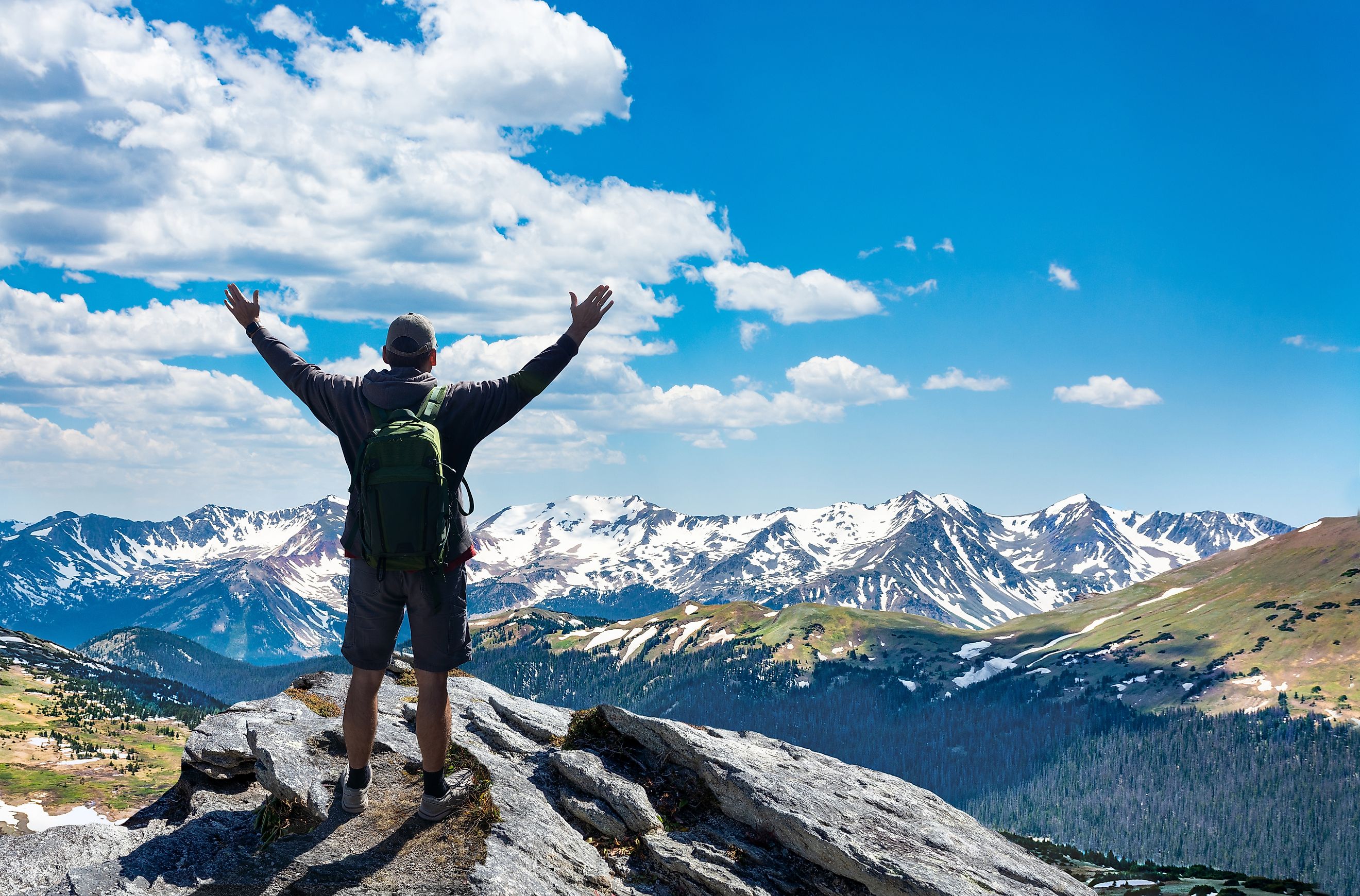 Hiker with arms raised in triumph standing atop a mountain in Rocky Mountain National Park, Colorado.