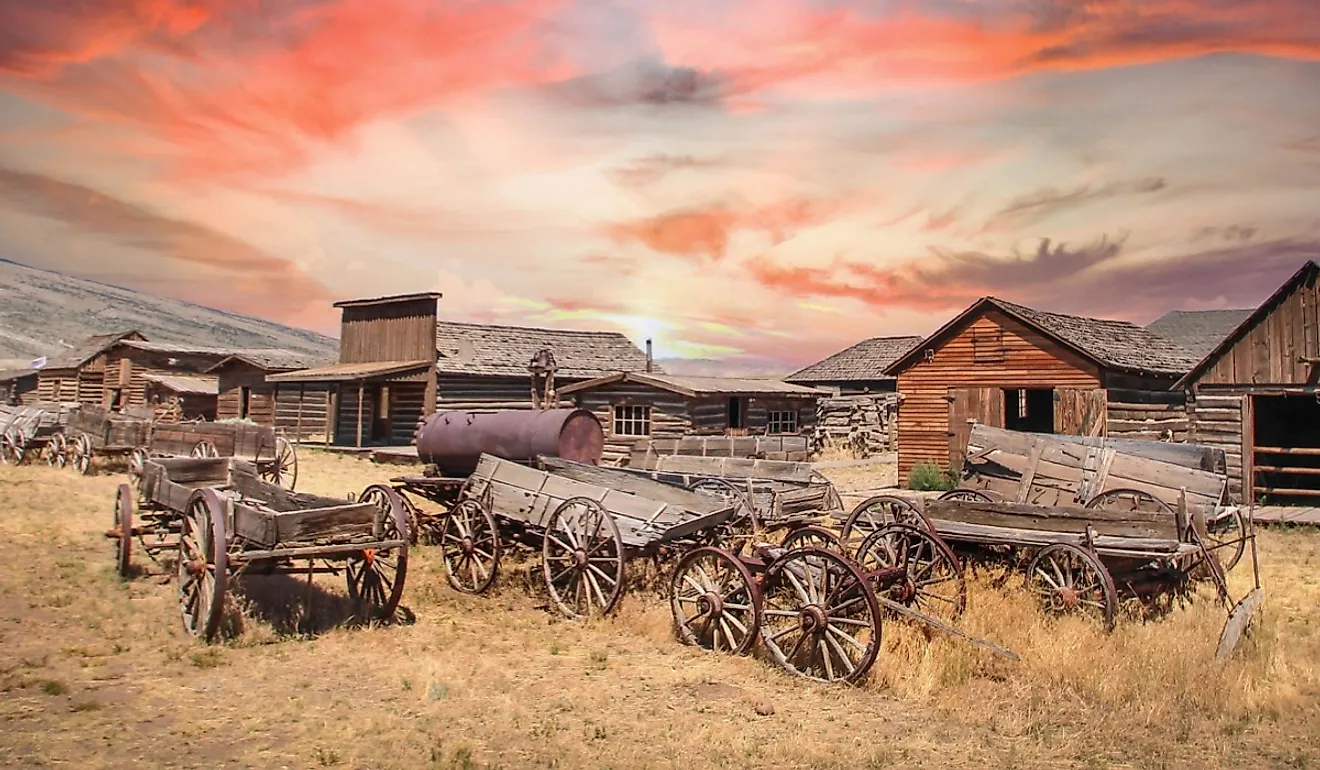 Antique wheels and wagons at a ranch in Cody, Wyoming, under a rising sun.