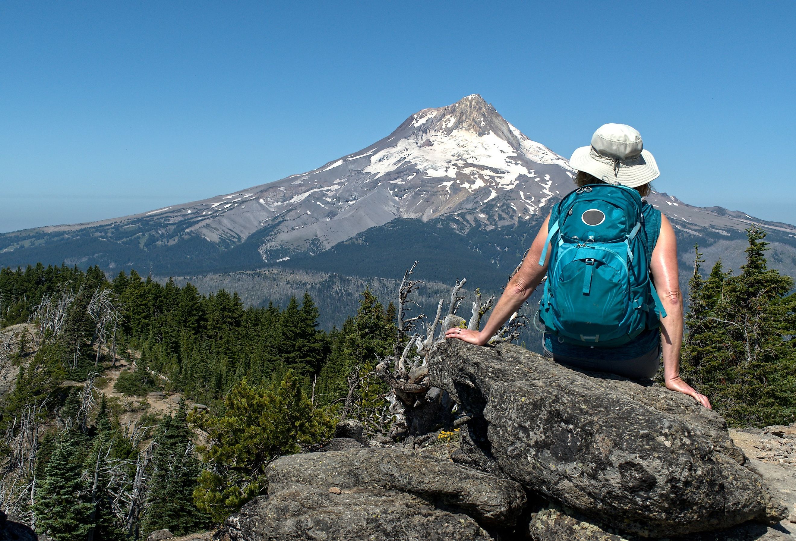 A mature woman hiker sites on a rock with her back to us and enjoys the view of Mt. Hood, Oregon.