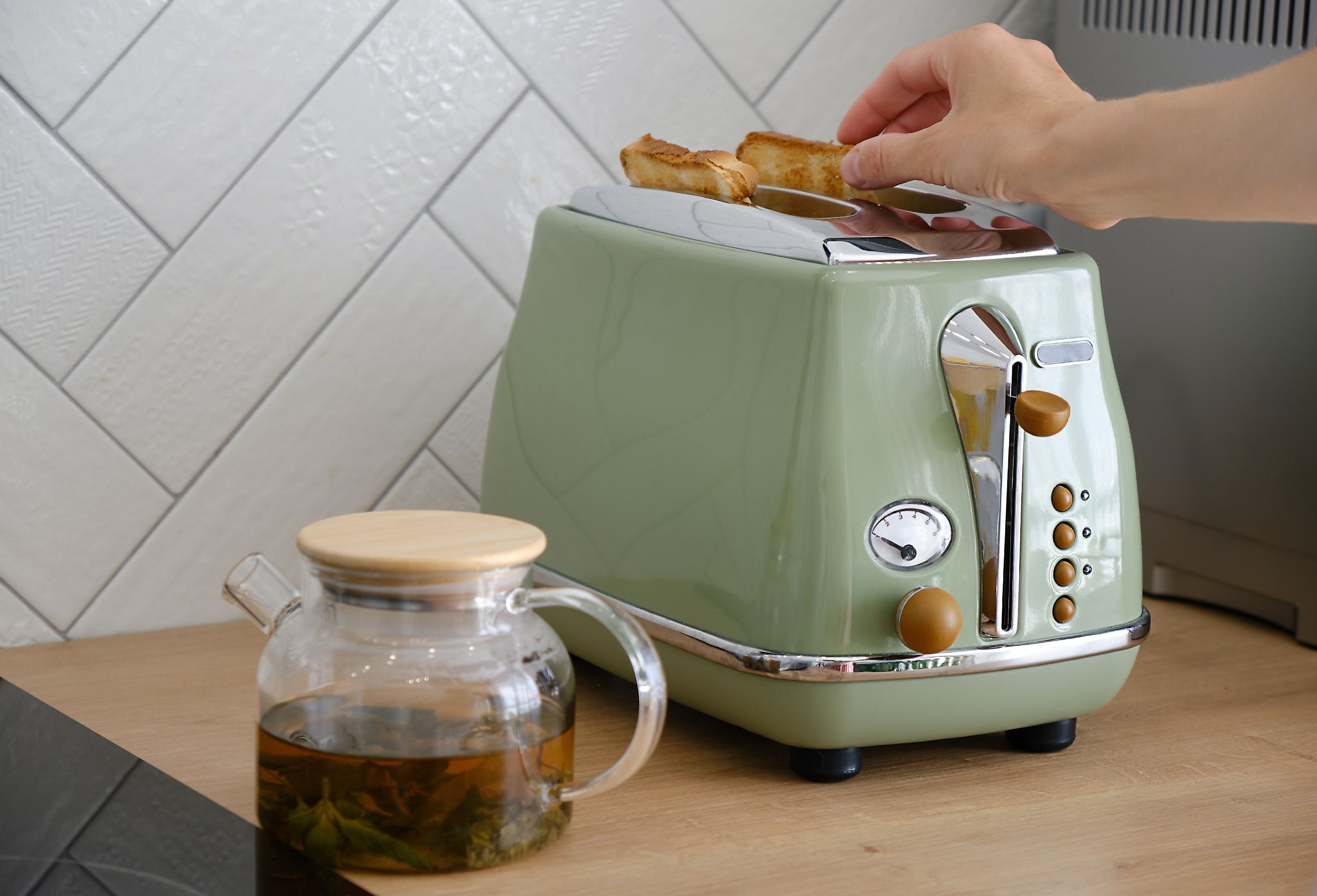 Woman using a retro green toaster on the countertop with a cup of tea.