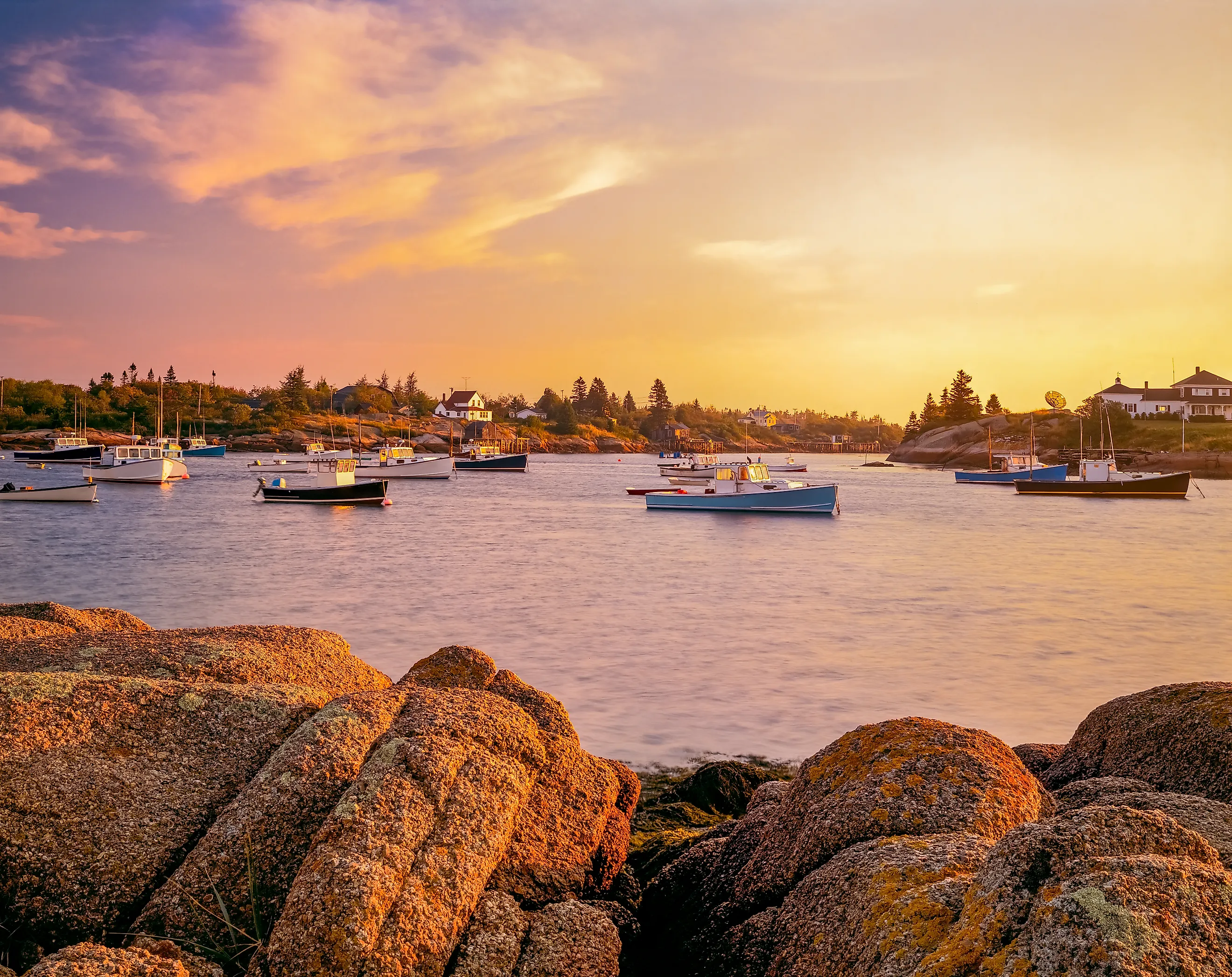 Rocky shoreline surrounds fishing boats in the Corea Harbor at sunset in Maine.