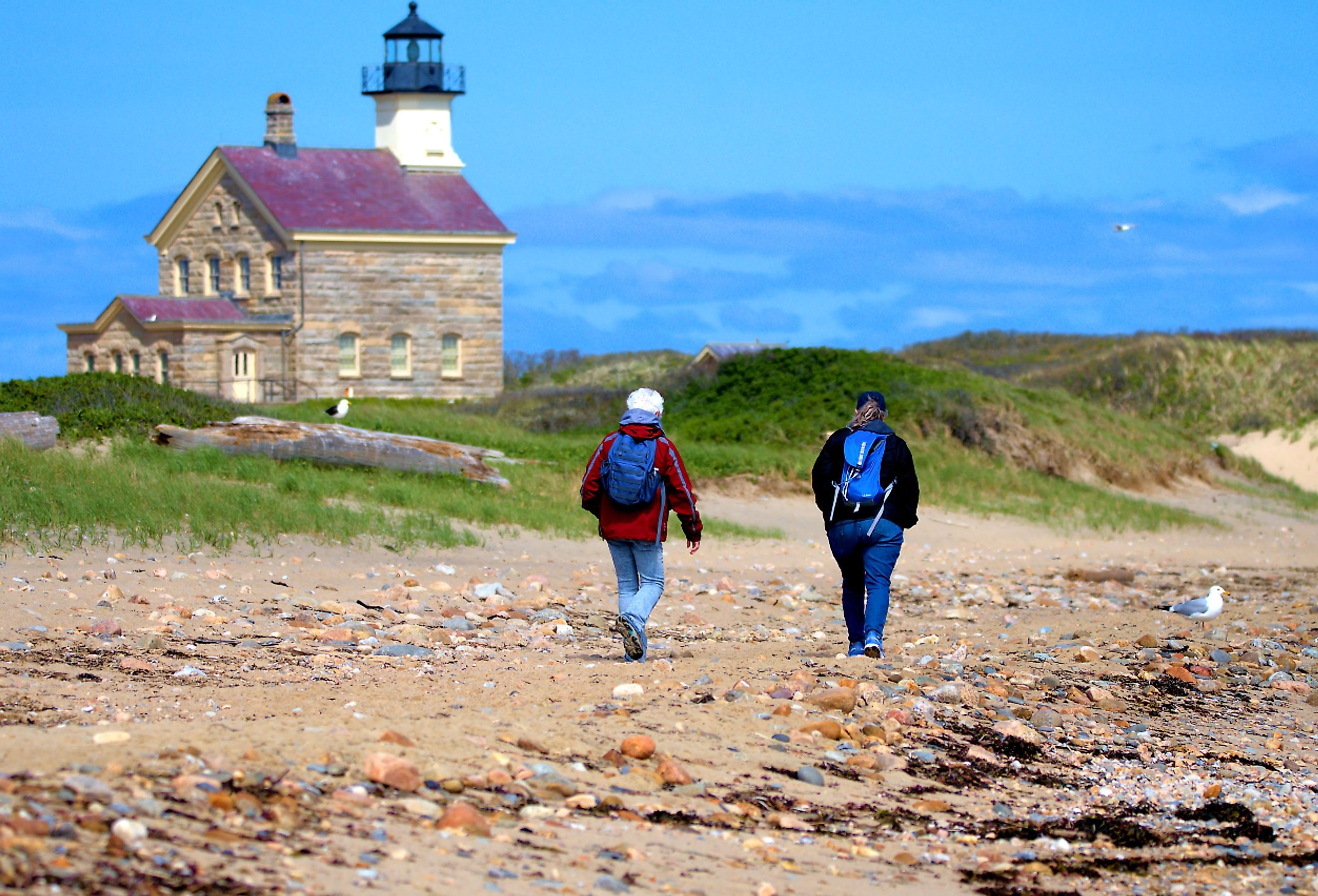 Pair of women walk the shoreline past the historic North Lighthouse on Block Island, New Shoreham, Rhode Island. Image credit Ray Geiger via Shutterstock