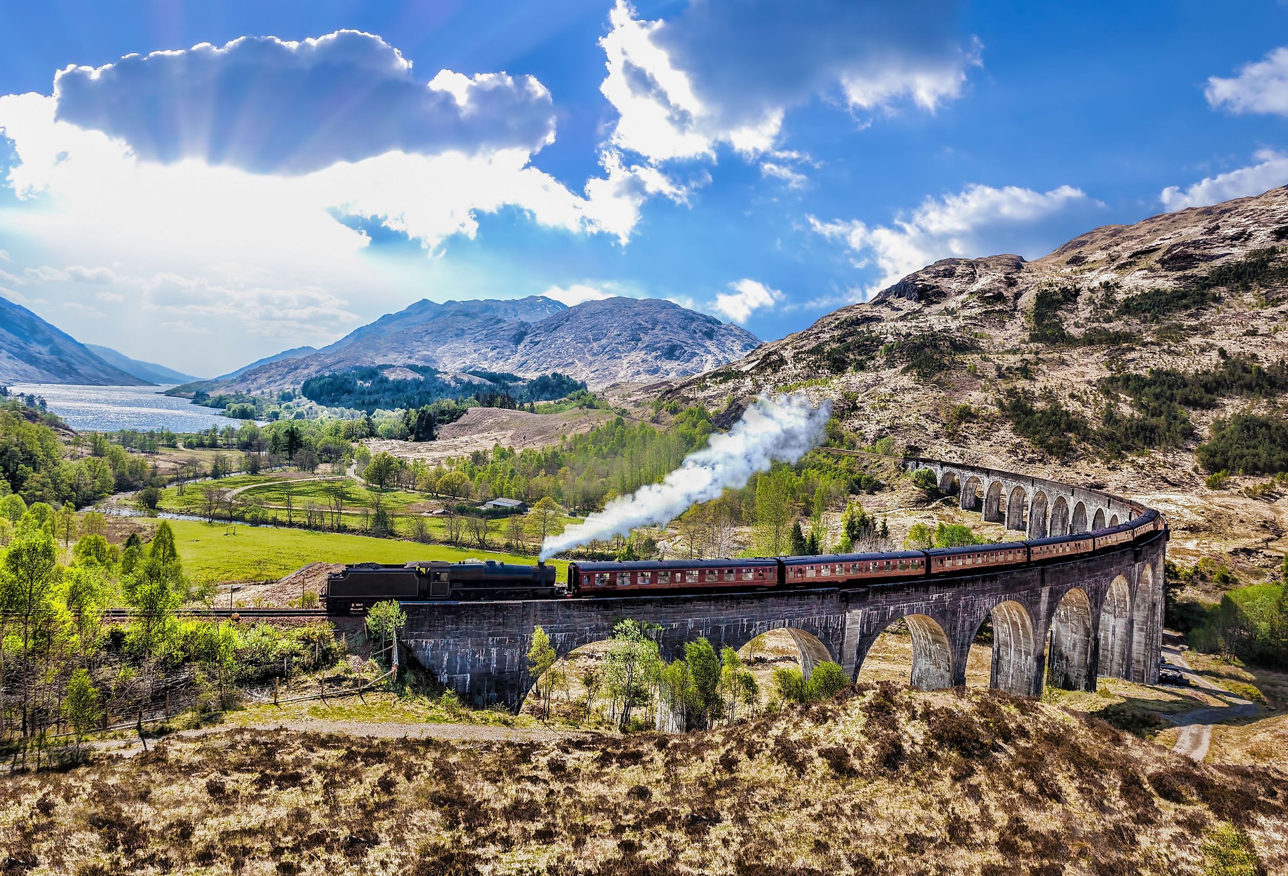 Glenfinnan Railway Viaduct in Scotland with the Jacobite steam train against sunset over lake. Image credit: Tomas Marek via Shutterstock