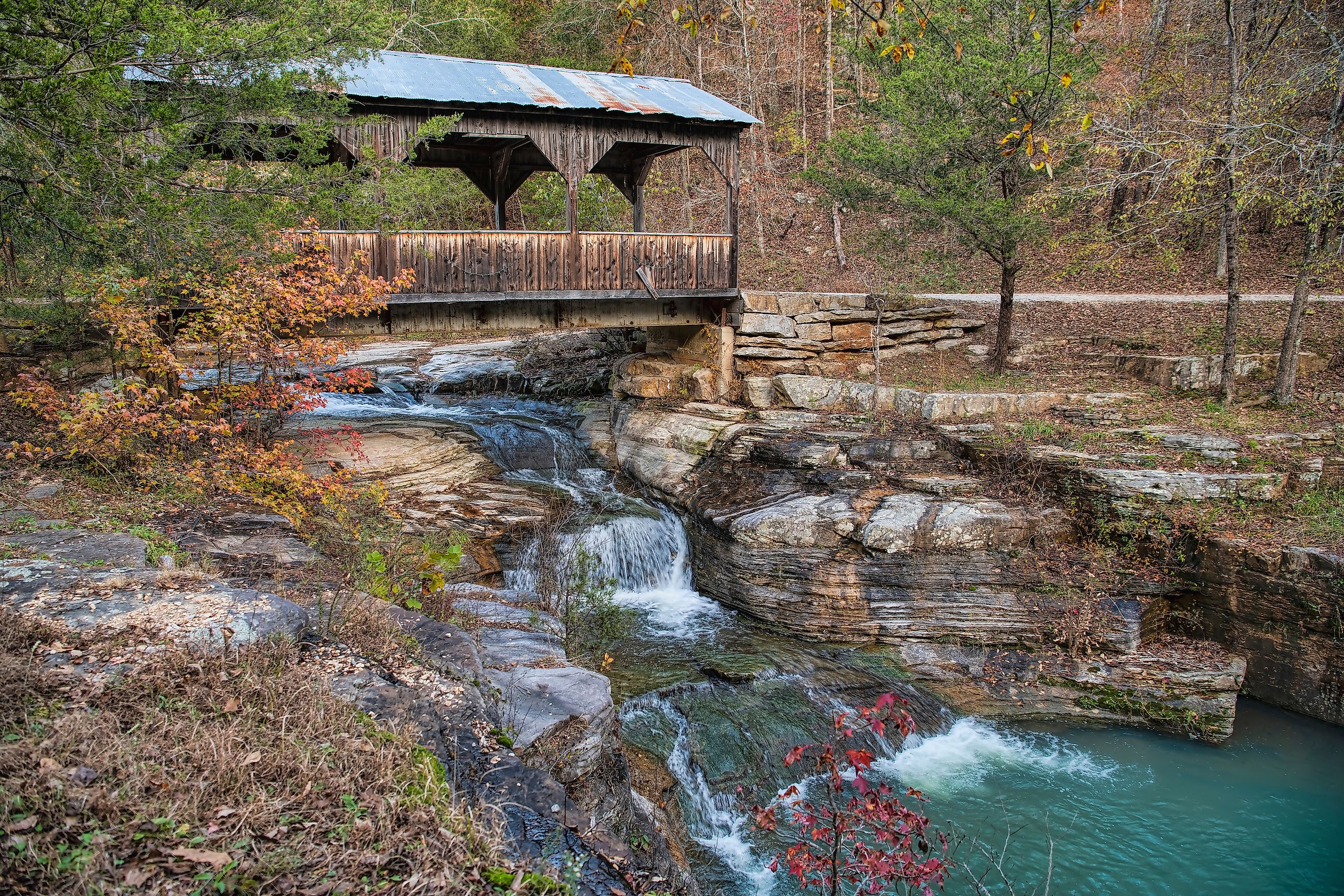 Covered bridge over cascading waterfall in fall in Ponca, Arkansas.