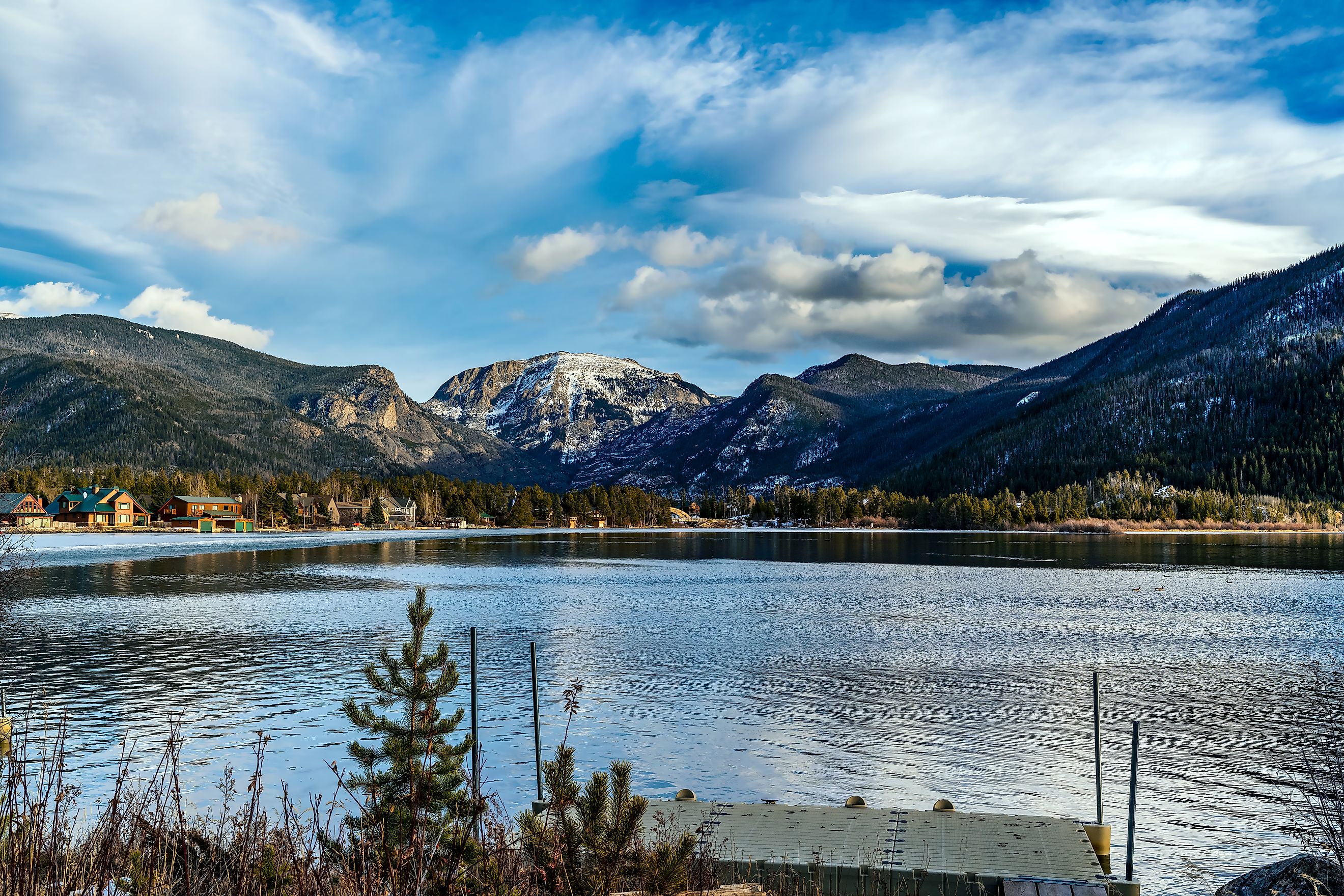 Views of the snow-covered mountain tops of the Rocky Mountains across a still, smooth lake in Grand Lake, Colorado