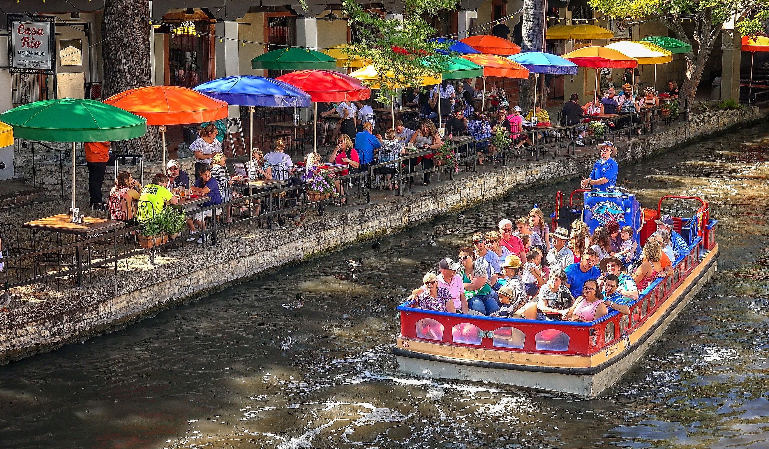 A tour boat passes a restaurant along the historic San Antonio River Walk. Editorial credit: CrackerClips Stock Media / Shutterstock.com